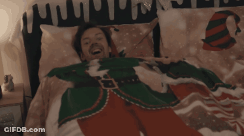 A Man In A Christmas Sweater Is Laying In A Bed GIF
