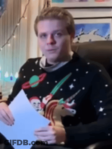 A Man In A Christmas Sweater Is Sitting In A Chair Holding A Piece Of Paper GIF