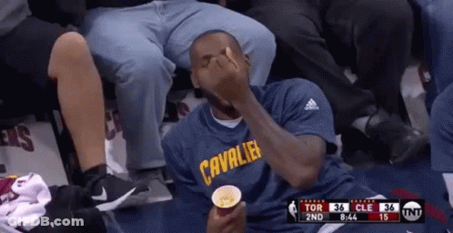 A Man In A Cleveland Cavaliers Shirt Is Sitting In A Stadium Eating Popcorn . GIF