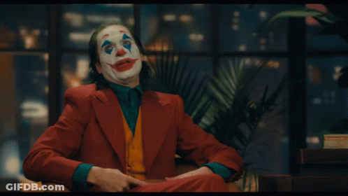 A Man In A Clown Costume Is Sitting In A Chair With His Mouth Open GIF