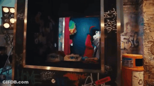 A Man In A Clown Costume Is Standing In A Box With Graffiti On The Wall . GIF