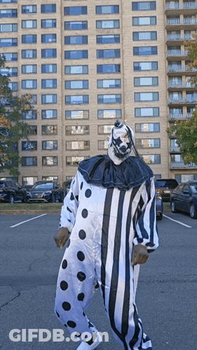 A Man In A Clown Costume Is Standing In A Parking Lot In Front Of A Tall Building GIF