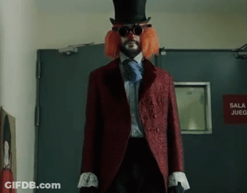 A Man In A Clown Costume Is Standing In Front Of A Red Sign That Says Sala Juego GIF