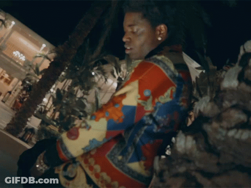 A Man In A Colorful Jacket Is Standing In Front Of A Building GIF