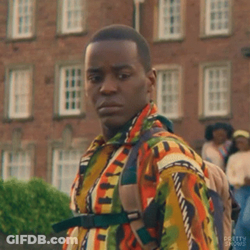 A Man In A Colorful Shirt And Backpack Is Standing In Front Of A Brick Building . GIF