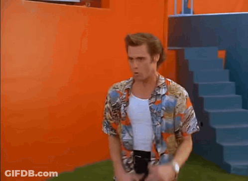 A Man In A Colorful Shirt And Black Pants Is Dancing In Front Of An Orange Wall And Stairs . GIF