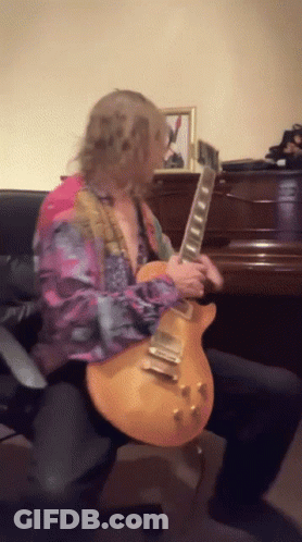 A Man In A Colorful Shirt Is Playing A Guitar In Front Of A Piano GIF