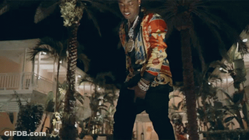 A Man In A Colorful Shirt Stands In Front Of Palm Trees At Night GIF