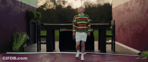 A Man In A Colorful Sweater And White Shorts Is Standing In Front Of A Table . GIF