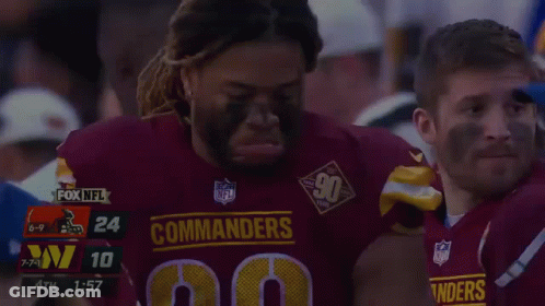 A Man In A Commanders Jersey Is Being Helped By Another Man GIF