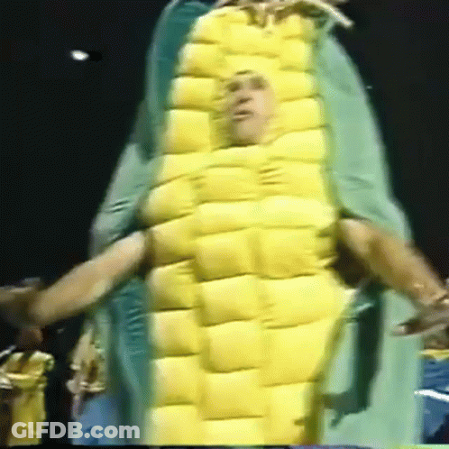 A Man In A Corn On The Cob Costume Is Being Held By Another Man GIF