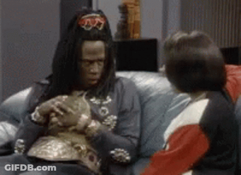 A Man In A Costume Is Sitting On A Couch Holding A Cat . GIF