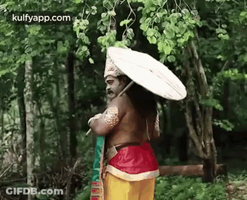 A Man In A Costume Is Standing In The Woods Holding An Umbrella . GIF