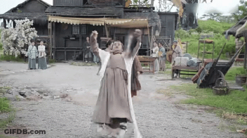 A Man In A Costume Is Standing On A Dirt Road Holding A Sword In His Hands . GIF