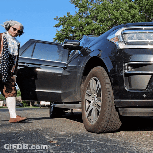 A Man In A Costume Stands Next To A Black Suv GIF