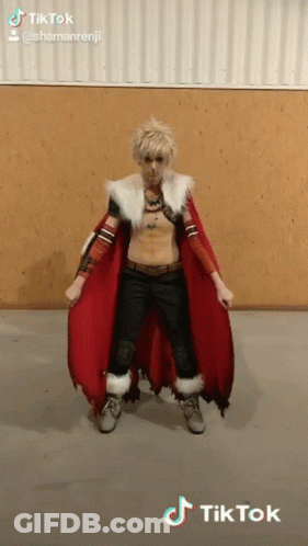 A Man In A Costume With A Red Cape Is Standing In Front Of A Wooden Wall . GIF