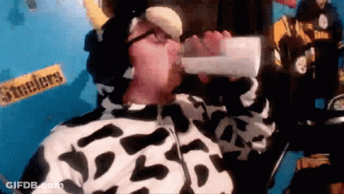 A Man In A Cow Costume Drinks From A Bottle GIF