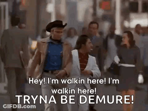 A Man In A Cowboy Hat And A White Suit Is Walking Down A Street With A Woman . GIF