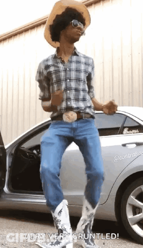 A Man In A Cowboy Hat And Cowboy Boots Is Standing Next To A Car . GIF
