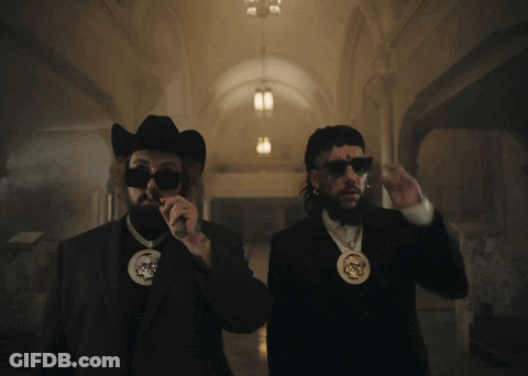A Man In A Cowboy Hat And Sunglasses Stands Next To Another Man GIF