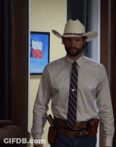 A Man In A Cowboy Hat And Tie Stands In Front Of A Painting Of A Texas Flag GIF