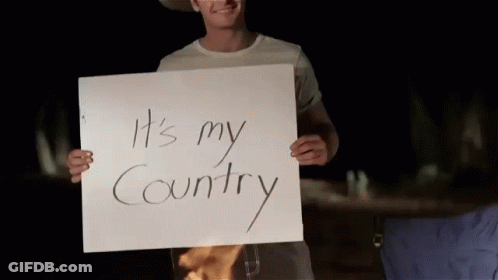A Man In A Cowboy Hat Holds A Sign That Says It 'S My Country GIF