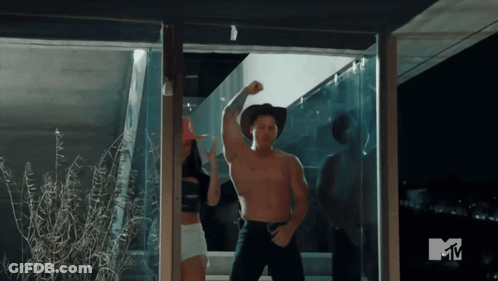 A Man In A Cowboy Hat Is Flexing His Muscles In Front Of A TV Screen That Says Mtv GIF