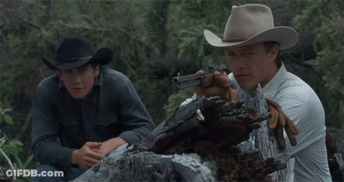 A Man In A Cowboy Hat Is Holding A Gun Next To Another Man GIF