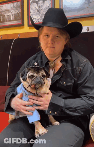 A Man In A Cowboy Hat Is Holding A Pug GIF