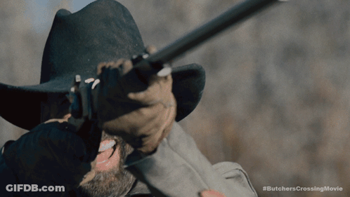 A Man In A Cowboy Hat Is Holding A Rifle With The Hashtag #Butcherscrossingmovie Below Him GIF
