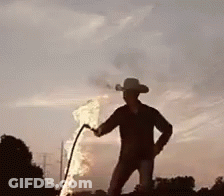 A Man In A Cowboy Hat Is Holding A Torch In Front Of A Flame . GIF