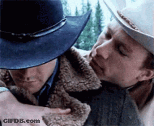 A Man In A Cowboy Hat Is Hugging Another Man In A Fur Coat GIF