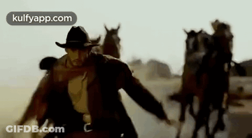 A Man In A Cowboy Hat Is Leading A Herd Of Horses Through A Desert . GIF