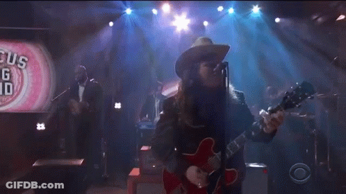 A Man In A Cowboy Hat Is Playing A Red Guitar GIF