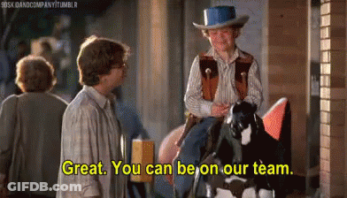 A Man In A Cowboy Hat Is Riding A Horse While Another Man Stands Behind Him . GIF
