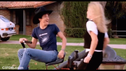 A Man In A Cowboy Hat Is Riding A Lawn Mower GIF
