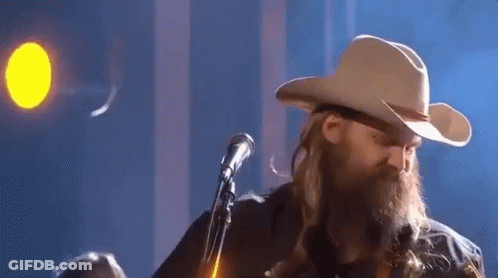 A Man In A Cowboy Hat Is Singing Into A Microphone . GIF