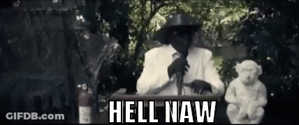 A Man In A Cowboy Hat Is Standing At A Podium With A Statue Of A Monkey . GIF