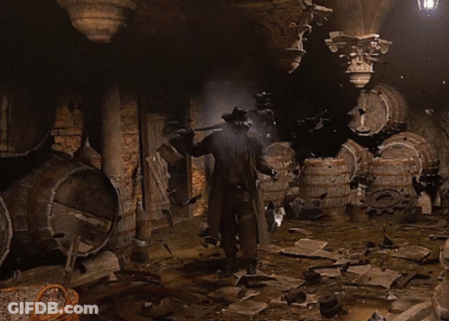 A Man In A Cowboy Hat Is Standing In A Dark Room With Barrels GIF