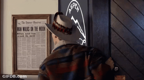 A Man In A Cowboy Hat Is Standing In Front Of A Framed Newspaper That Says Man Walks On The Moon GIF
