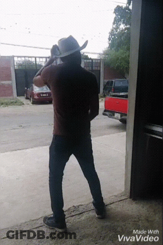 A Man In A Cowboy Hat Is Standing Next To A Red Truck GIF