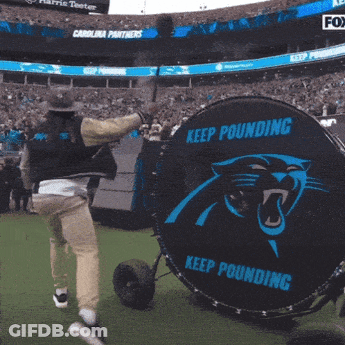 A Man In A Cowboy Hat Is Throwing A Baseball In A Stadium With A Banner For Harris Teeter GIF