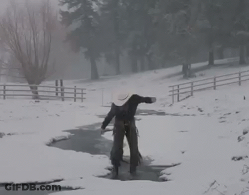 A Man In A Cowboy Hat Is Walking Across A Snow Covered Stream . GIF