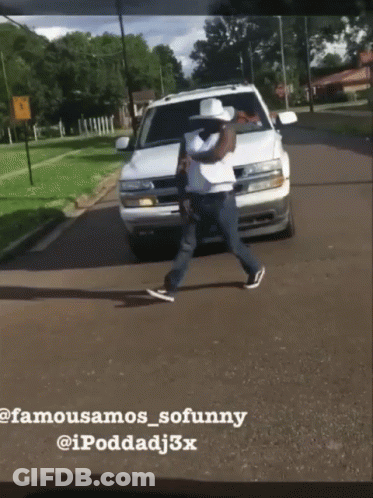 A Man In A Cowboy Hat Is Walking Across A Street In Front Of A White Suv GIF