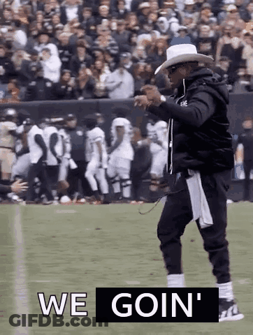 A Man In A Cowboy Hat Is Walking On A Football Field With The Words `` We Goin '' Written Above Him . GIF