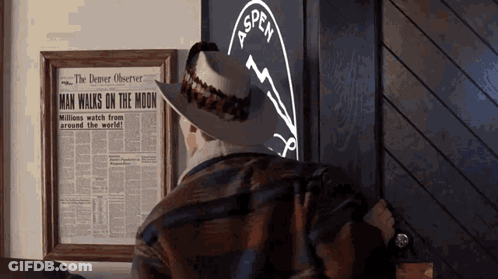 A Man In A Cowboy Hat Looks At A Framed Newspaper That Says Man Walks On The Moon GIF