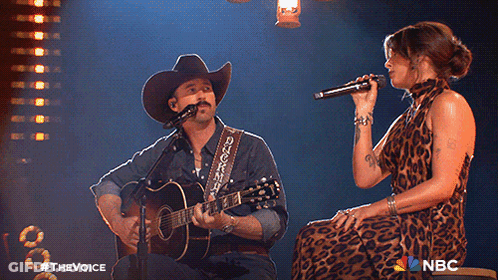 A Man In A Cowboy Hat Sings Into A Microphone While A Woman Sings Behind Him GIF