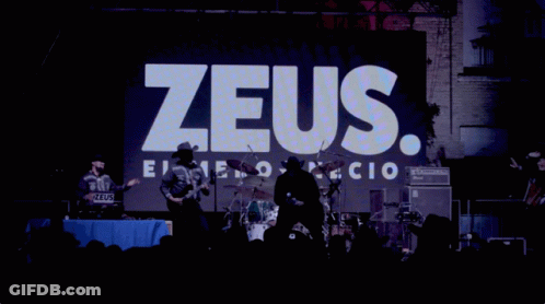 A Man In A Cowboy Hat Stands In Front Of A Zeus Sign GIF
