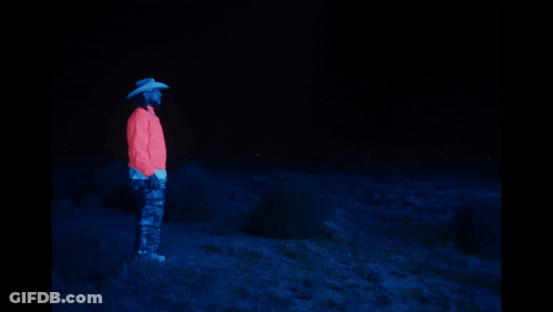 A Man In A Cowboy Hat Stands Next To A Glowing Horse In The Dark GIF