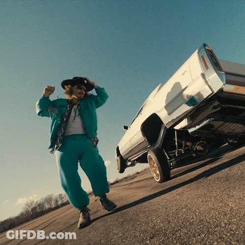 A Man In A Cowboy Hat Stands Next To A White Car On Its Rear Wheels GIF